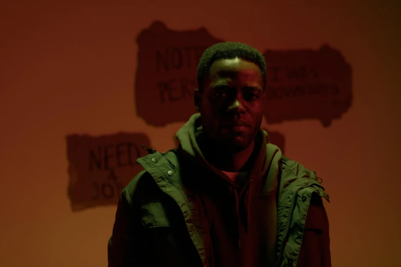 a man standing in front of a wall with signs on it, an album cover, pexels contest winner, serial art, kevin hart, standing in a dimly lit room, high resolution movie still, grime