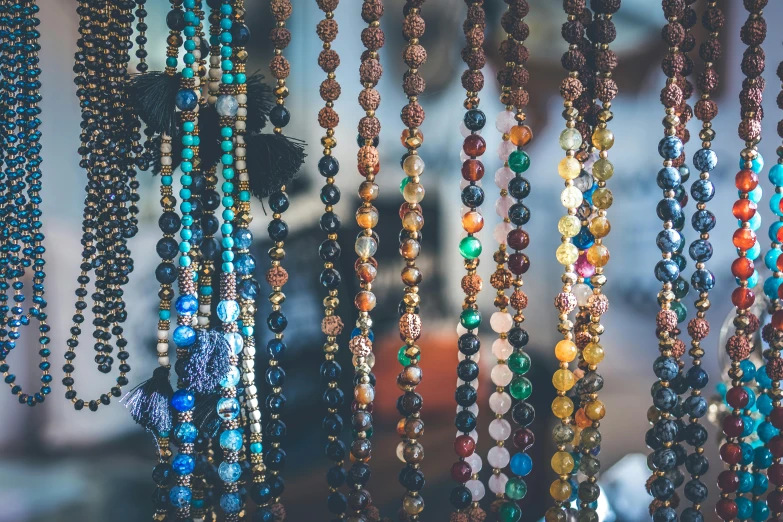 a close up of many different colored beads, trending on pexels, chains hanging from ceiling, shop window for magical weapons, hippie fashion, black jewellery