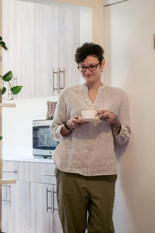 a woman standing in a kitchen holding a bowl, by Elizabeth Durack, trending on reddit, non-binary, wearing a linen shirt, architect, drinking tea