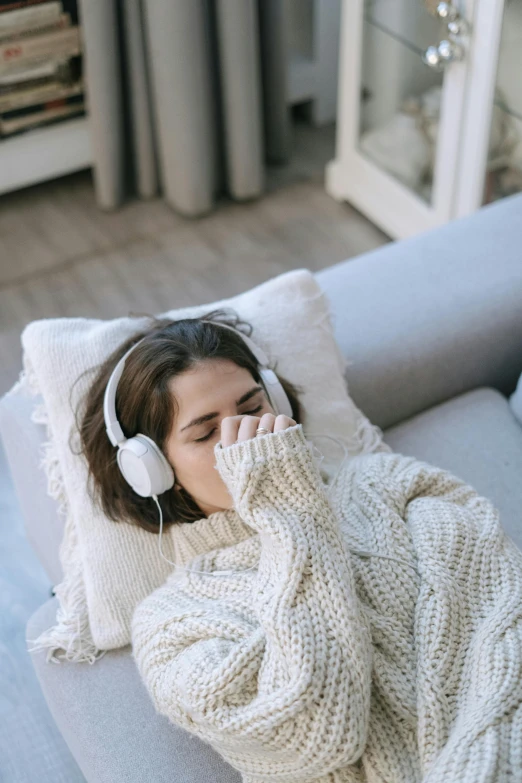 a woman laying on a couch with headphones on, trending on pexels, romanticism, wearing casual sweater, cold as ice! 🧊, coughing, comfy chairs