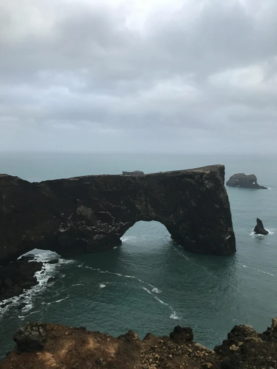 a man standing on top of a cliff next to the ocean, massive arch, slight overcast weather, photo taken in 2018, nina tryggvadottir