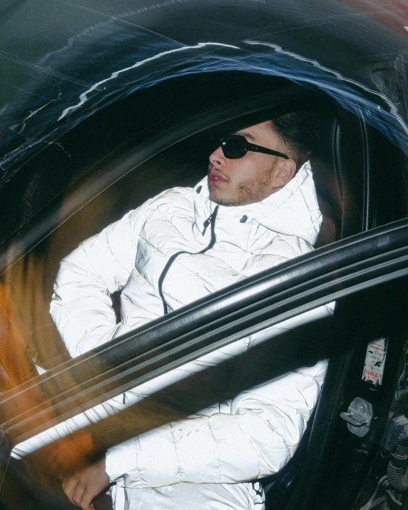 a man sitting in the driver's seat of a car, an album cover, inspired by Elsa Bleda, model wears a puffer jacket, matt white ice color armor, reflective sunglasses, passed out
