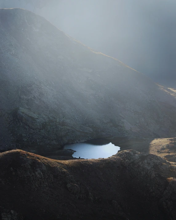 a large body of water sitting on top of a mountain, inspired by Michal Karcz, unsplash contest winner, small pond, light grey mist, looking down from above, wales