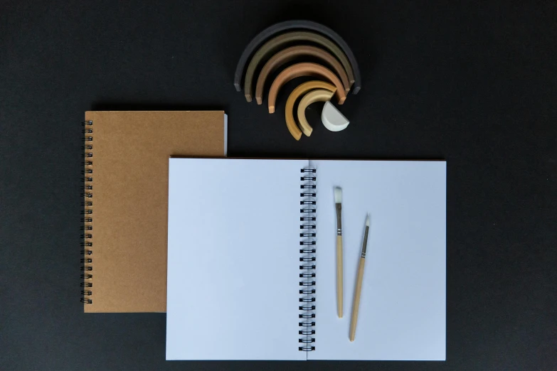 a spiral notebook sitting on top of a table next to a pen, a drawing, inspired by Leonardo da Vinci, process art, white ceramic shapes, with a wooden stuff, product introduction photo, arcs