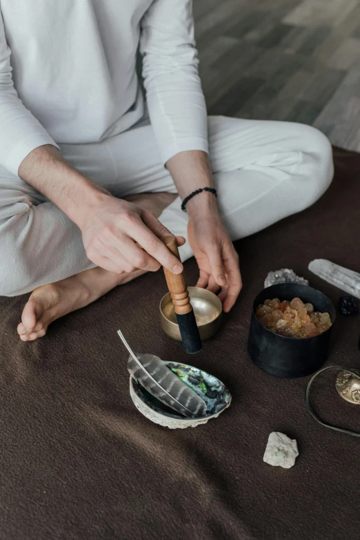 a woman sitting on the floor with a bowl of food, by Julia Pishtar, trending on pexels, renaissance, large obsidian crystals, music instrument in hand, healing tubes, holding a bell