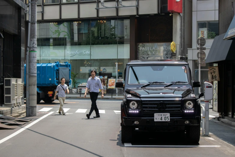 a black truck driving down a street next to tall buildings, unsplash, auto-destructive art, in karuizawa, land rover defender, people walking around, 🚿🗝📝