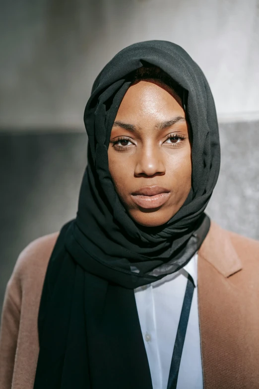 a woman wearing a black scarf and a brown coat, by Arabella Rankin, pexels contest winner, hurufiyya, androgynous face, islamic, black woman, promotional image