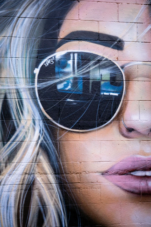 a painting of a woman with sunglasses on the side of a building, graffiti art, trending on pexels, close up of a blonde woman, perfectly shaded face, wall mural, high angle close up shot