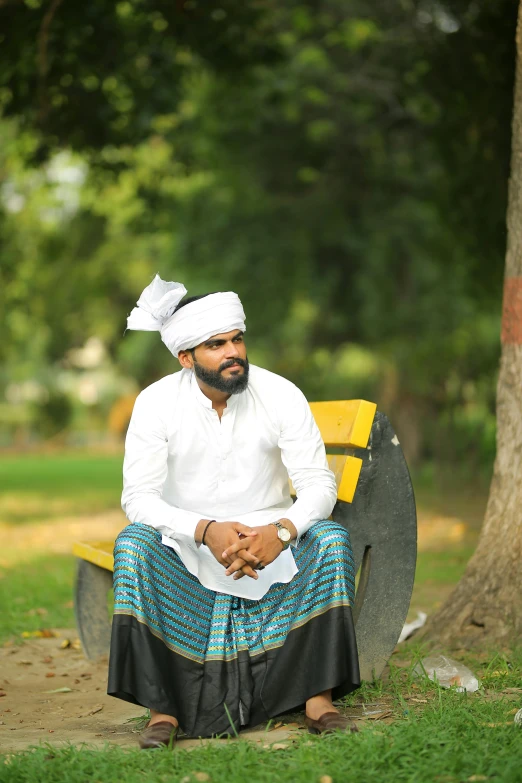 a man sitting on a bench in a park, an album cover, inspired by Sardar Sobha Singh, hurufiyya, traditional dress, **cinematic, turban, pr shoot