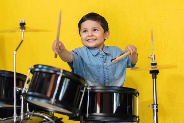 a young boy playing drums in front of a yellow wall, pexels contest winner, american barbizon school, avatar image, subject is smiling, 15081959 21121991 01012000 4k, tamborine