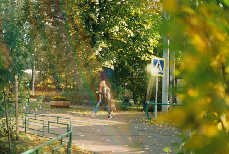 a woman walking down a path in a park, a picture, by Grytė Pintukaitė, green square, worksafe. cinematic, in the autumn, student