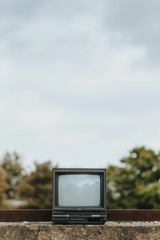 a small television sitting on top of a cement wall, unsplash, video art, trees in background, sky, vertical portrait, autumnal