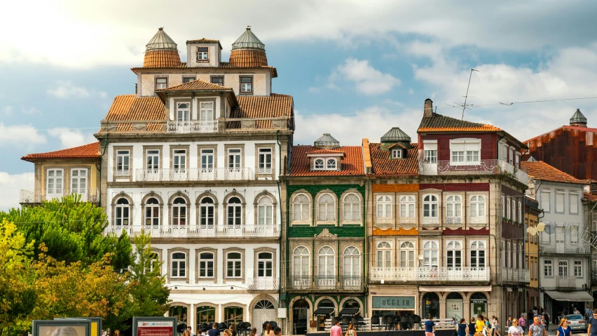 a group of people walking down a street next to tall buildings, inspired by Almada Negreiros, pexels contest winner, art nouveau, white houses, arrendajo in avila pinewood, square, viewed from the ocean