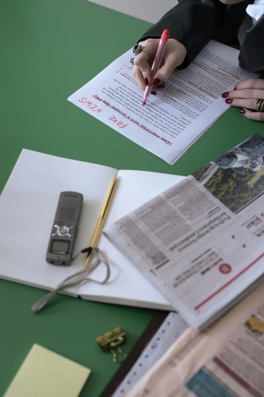 a woman sitting at a table with papers and a cell phone, private press, educational supplies, middle shot, red writing, news coverage