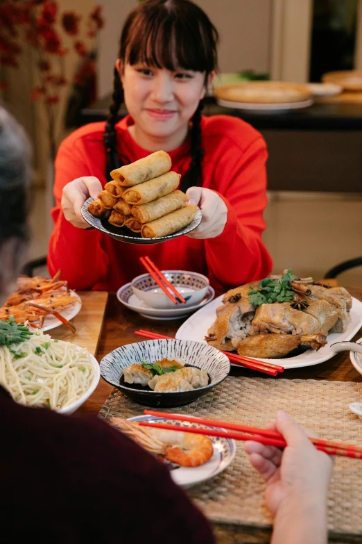 a woman sitting at a table with plates of food, inspired by Cui Bai, holiday season, plated arm, offering a plate of food, battered