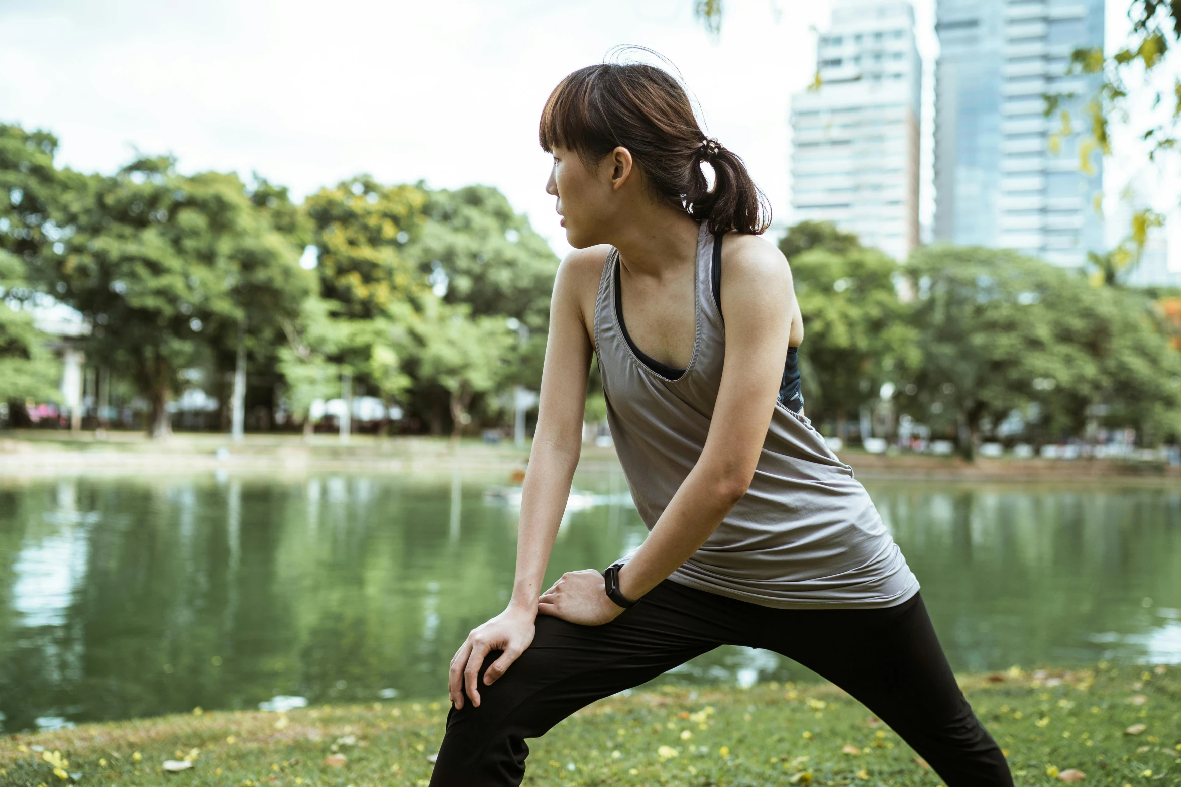 a woman doing a yoga pose in front of a body of water, happening, in a city park, gemma chan, looking to the side, sweat and labour