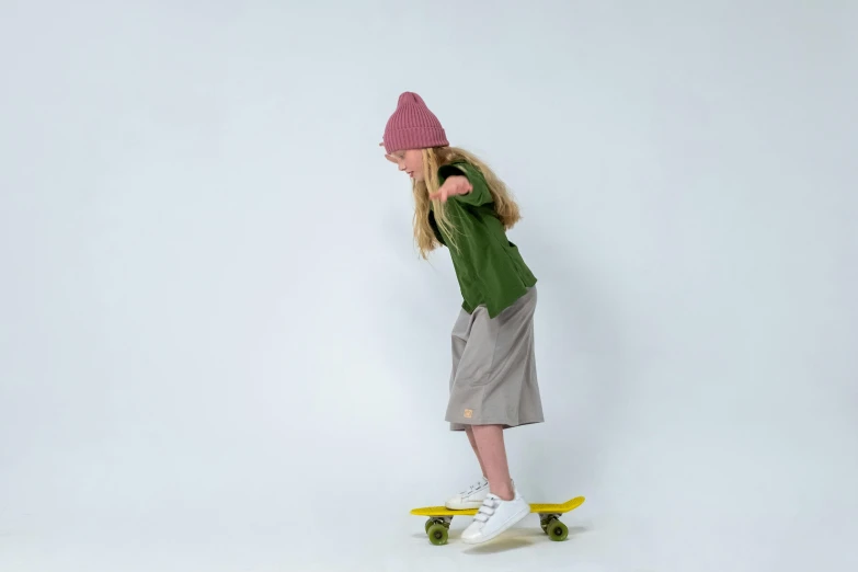 a little girl riding a skateboard on a white surface, by Lucette Barker, dribble, baggy clothing and hat, olive green, official product photo, for kids