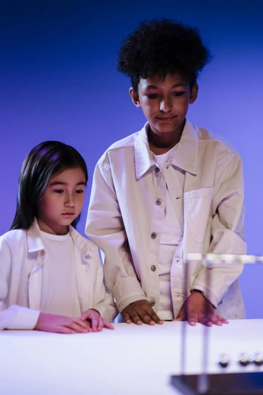 a couple of kids that are standing in front of a table, pexels, interactive art, with a lab coat, lighting, slide show, gif