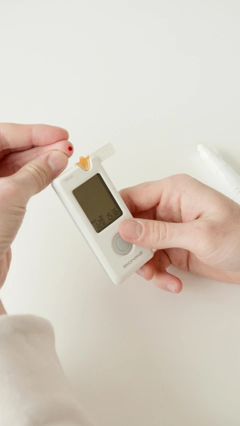 a close up of a person holding an electronic device, offering the viewer a pill, on a white table, square, press shot