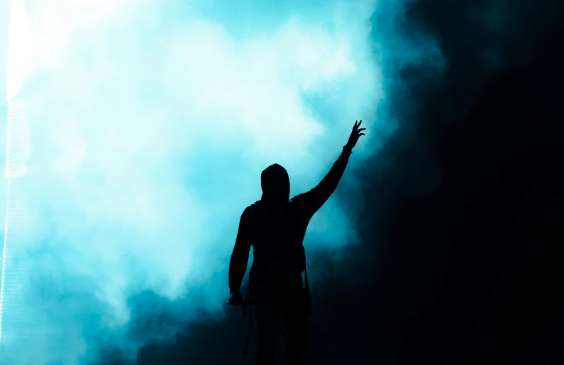 a silhouette of a man holding a tennis racquet, pexels contest winner, conceptual art, cyan fog, rapping on stage at festival, indistinct man with his hand up, background ( dark _ smokiness )