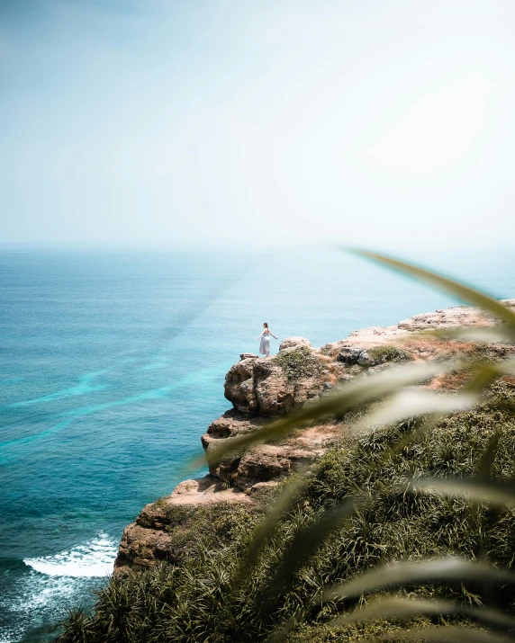 a man standing on top of a cliff next to the ocean, pexels contest winner, sumatraism, mermaids in distance, an arab standing watching over, bella poarch, lush vista