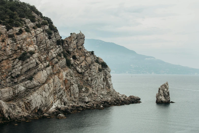 a couple of rocks sitting on top of a body of water, pexels contest winner, steep cliffs, gulf of naples, overcast lighting, conde nast traveler photo