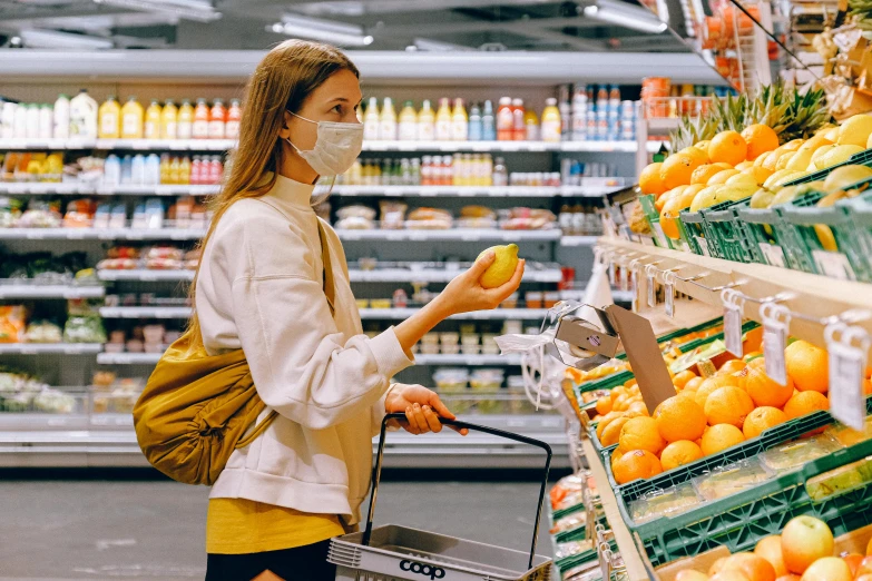 a woman wearing a face mask while shopping in a grocery store, a picture, by Julia Pishtar, pexels, holding a tangerine, white and yellow scheme, 🦩🪐🐞👩🏻🦳, sydney hanson