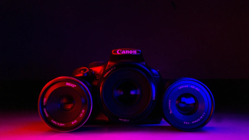 a couple of cameras sitting on top of a table, by Tom Carapic, red and blue black light, background canon, purple and red, canon dslr