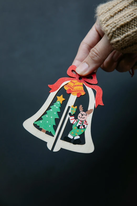 a person holding a christmas bell ornament, a cartoon, inspired by Ernest William Christmas, cut out of cardboard, middle shot, inside, detailed product shot