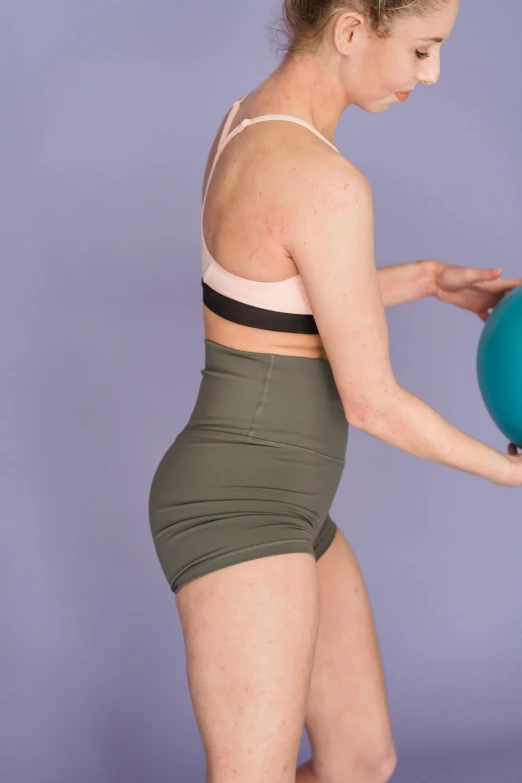 a woman in grey shorts holding a blue ball, crop yoga short, eighties-pinup style, outfit photograph, green body