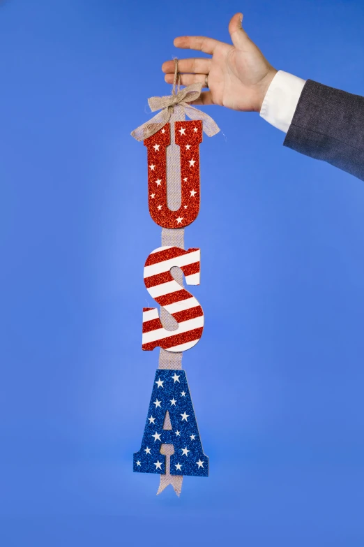 a close up of a person holding an american flag ornament, by Julia Pishtar, international typographic style, 7 feet tall, suit made of stars, wooden art toys on base, dollar sign