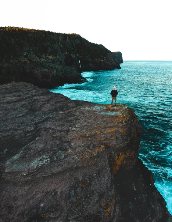 a man standing on top of a cliff next to the ocean, bella poarch, standing next to water, sharp cliffs, rhys lee