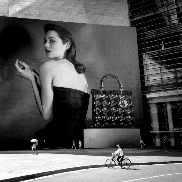 a black and white photo of a woman on a bike, inspired by Peter Basch, street art, emma watson modeling for gucci, on madison avenue, a gigantic wall, photograph credit: ap