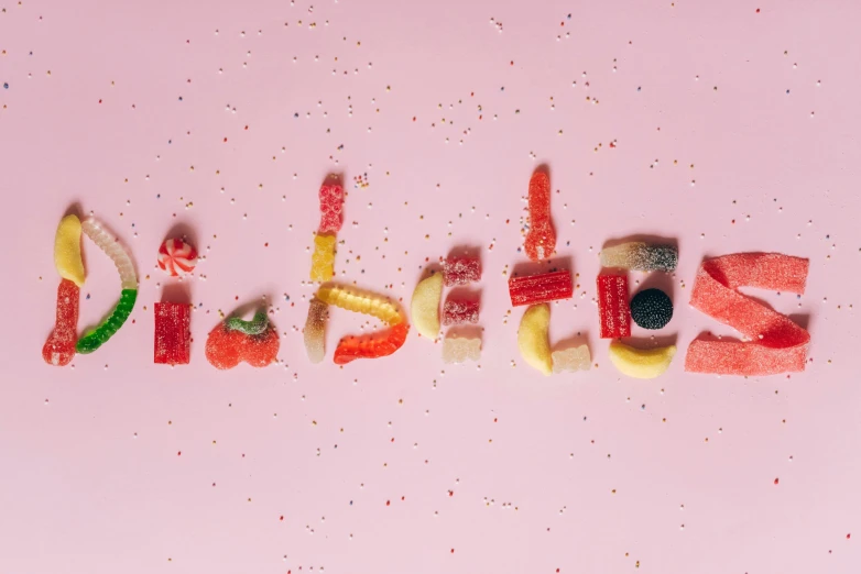 a word made out of candy sitting on top of a pink surface, by Isabel Naftel, pexels, letterism, eating rotting fruit, isabella, 🍸🍋, folds of belly flab
