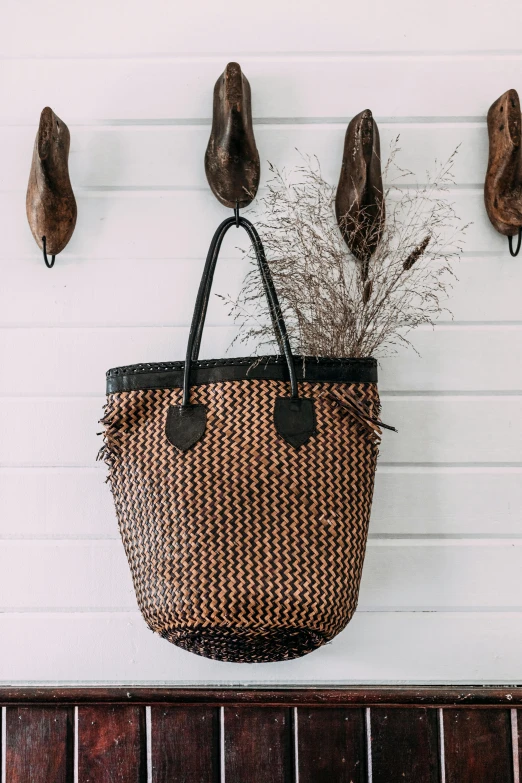 a wicker basket hanging on a wall, a picture, by Nina Hamnett, unsplash, hurufiyya, black and auburn colour pallet, bag, ultra detailed. style of arrival, kete butcher