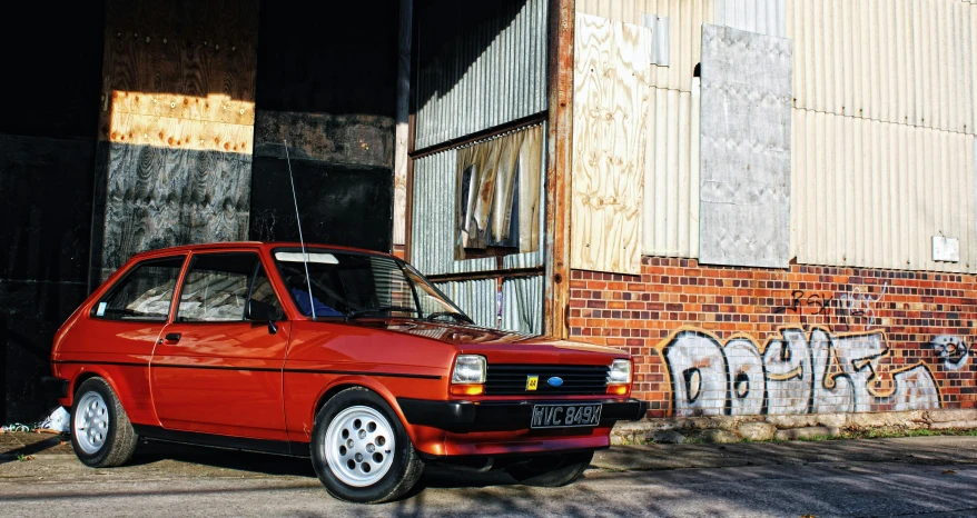 a red car parked in front of a building, an album cover, inspired by Ford Madox Brown, unsplash, 1985 cheverlot k20 c10, in front of a garage, bathed in golden light, lada