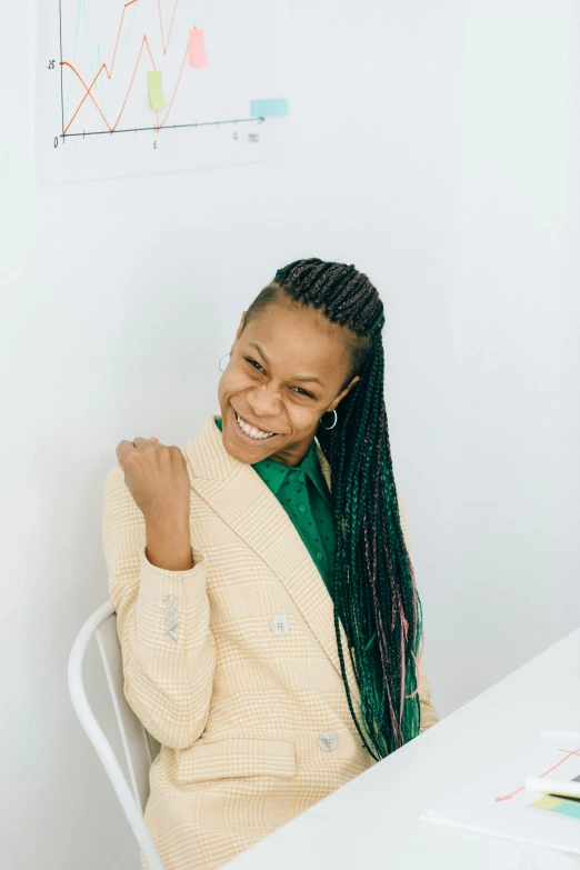 a woman sitting at a table in front of a computer, trending on pexels, black arts movement, wearing green suit, smiling kindly, kirsi salonen, woman with braided brown hair