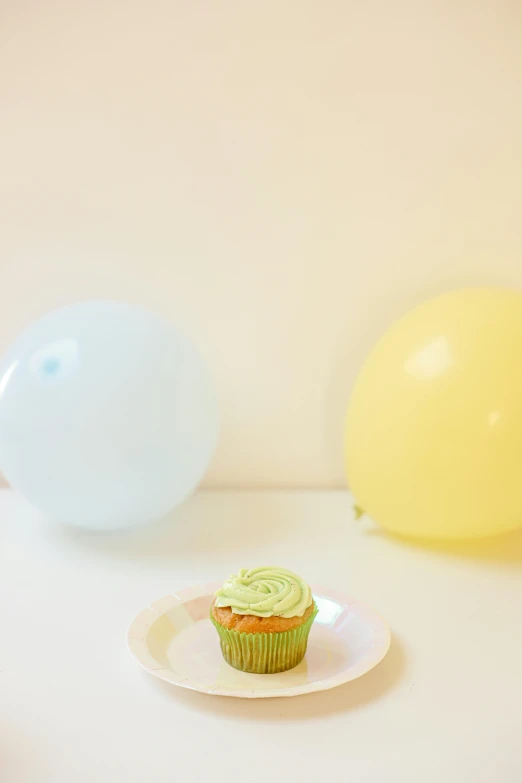 a cupcake sitting on top of a plate next to balloons, light green, promo image, minimalist photo, at the party