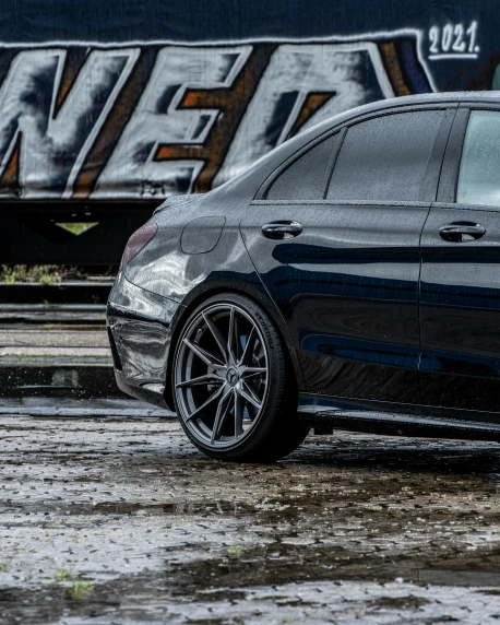 a black car parked in front of a train, profile image, slick wet walls, mercedez benz, deep dish wheels