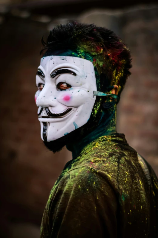 a man wearing a mask with paint all over his face, a colorized photo, inspired by Banksy, trending on pexels, action painting, portrait of a vigilante, the god of mischief, random colors, innocent look