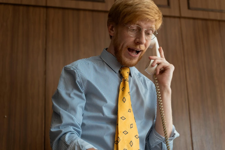 a man in a blue shirt and yellow tie talking on a phone, looks like domhnall gleeson, ricky berwick, press shot, blippi