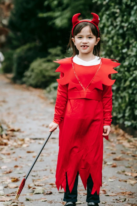 a little girl dressed in a red devil costume, inspired by Lucas Cranach the Elder, pokemon trainer outfit, with a walking cane, maisie williams, clifford the big red dog