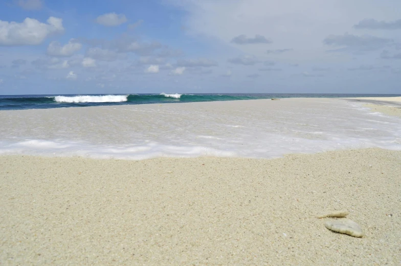 a large body of water sitting on top of a sandy beach, by Carey Morris, pexels contest winner, ocean spray, indonesia, vanilla, 3 / 4 wide shot