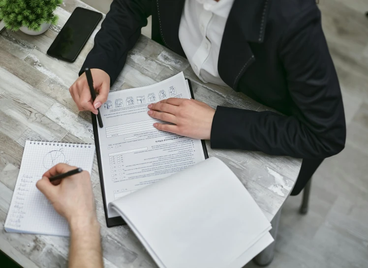 two people sitting at a table with notebooks and papers, pexels contest winner, selling insurance, a man wearing a black jacket, high level of details, listing image