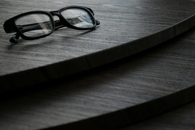 a pair of glasses sitting on top of a wooden table, unsplash, photorealism, bog oak, gunmetal grey, wooden stairs, fineline detail