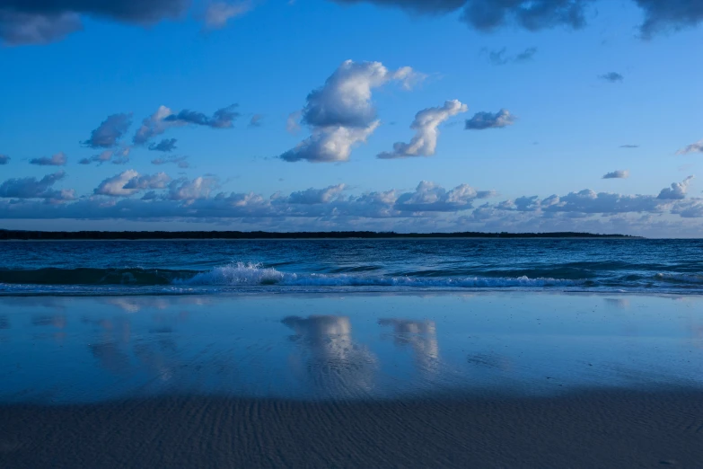 a man riding a surfboard on top of a sandy beach, giant clouds, blue reflections, on the beach at noonday, dreamtime