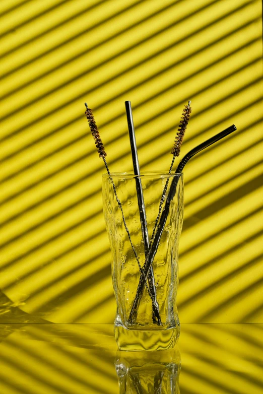 a glass filled with straws sitting on top of a table, by Carey Morris, pexels, photorealism, yellow and black, made of brushed steel, a pair of ribbed, sun and shadow