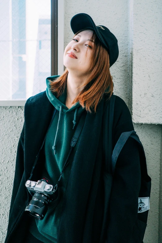 a woman with a camera leaning against a wall, by Miyamoto, unsplash, shin hanga, wearing an oversized hoodie, in a dark green polo shirt, あかさたなは on twitter, with hat