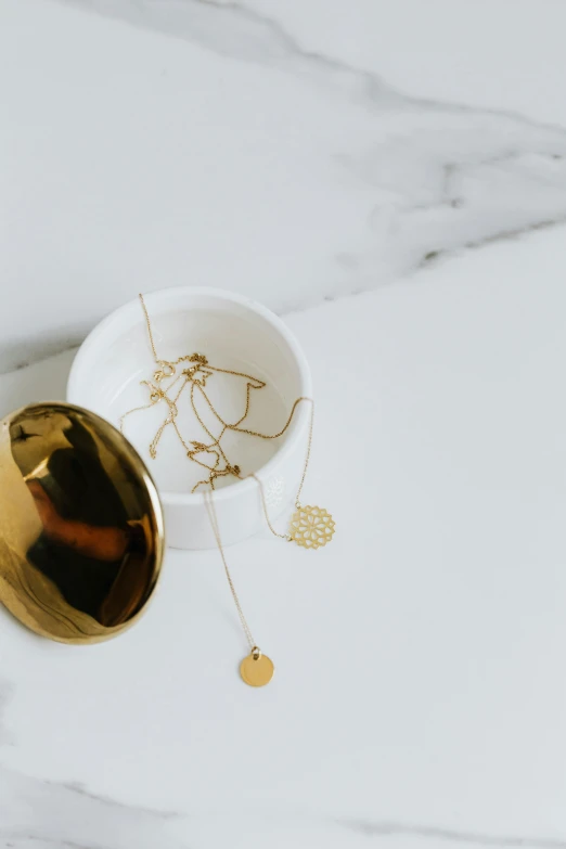 a cup sitting on top of a marble table, by Nicolette Macnamara, trending on pexels, minimalism, wearing several pendants, exposed gold wires, with small object details, clean white background