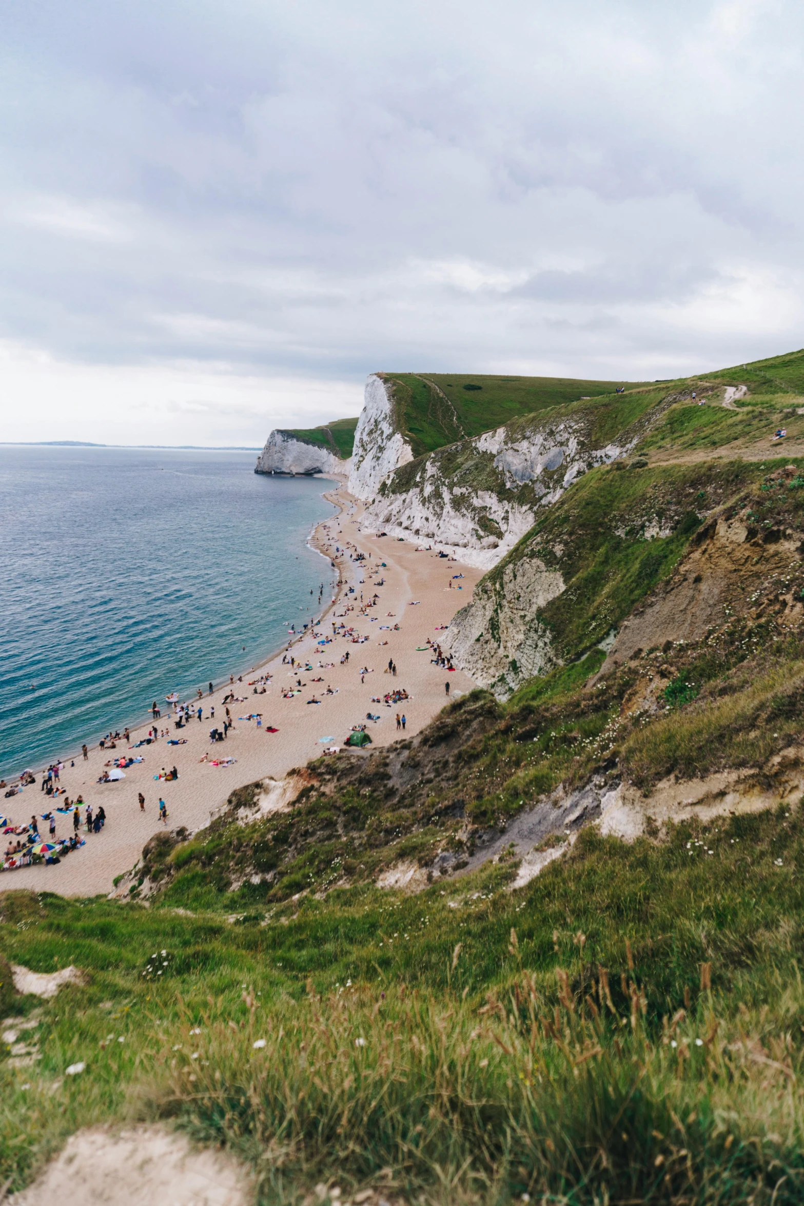 a group of people standing on top of a lush green hillside, by Rachel Reckitt, unsplash contest winner, renaissance, crowded beach, chalk cliffs above, square, autumn